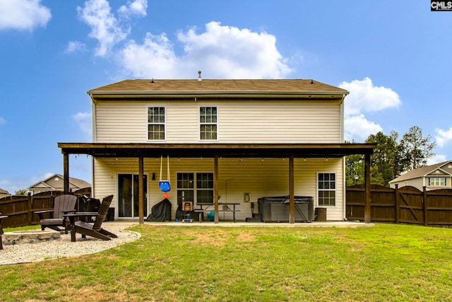 rear view of house with a hot tub, an outdoor fire pit, a lawn, and a patio area