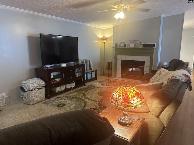 living room with crown molding, ceiling fan, a tiled fireplace, and a textured ceiling