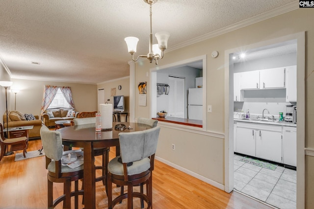 dining space with sink, crown molding, light hardwood / wood-style flooring, and a chandelier