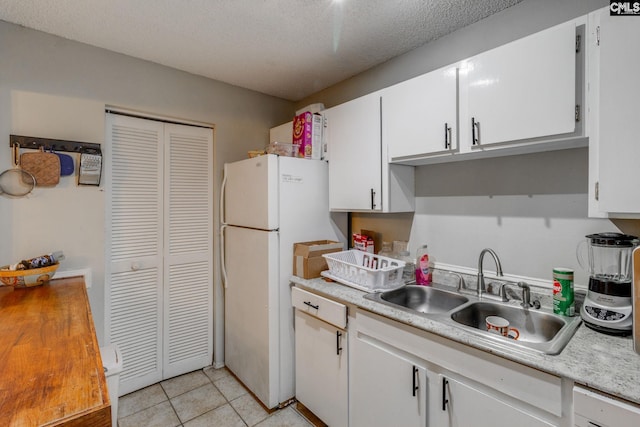 kitchen featuring light tile patterned flooring, white cabinetry, sink, white fridge, and a textured ceiling