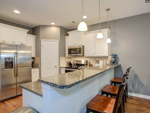 kitchen with appliances with stainless steel finishes, a breakfast bar, decorative light fixtures, white cabinetry, and kitchen peninsula