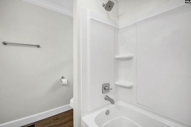 bathroom featuring ornamental molding, hardwood / wood-style floors, washtub / shower combination, and toilet