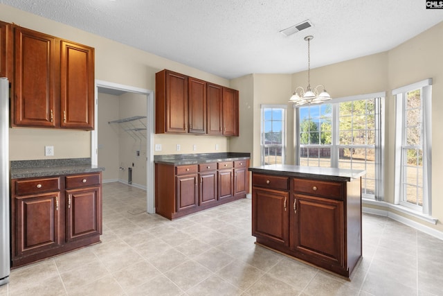 kitchen with hanging light fixtures, a kitchen island, a textured ceiling, and an inviting chandelier