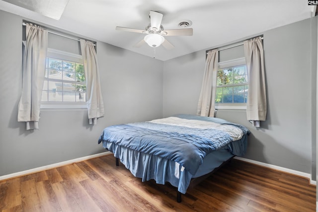 bedroom featuring ceiling fan, dark hardwood / wood-style flooring, and multiple windows