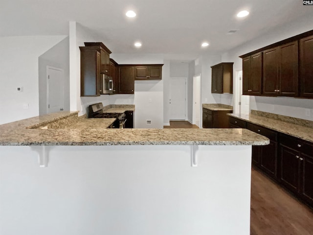 kitchen with dark brown cabinetry, a breakfast bar, light stone counters, kitchen peninsula, and stainless steel appliances