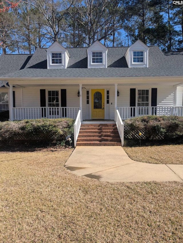 new england style home featuring a shingled roof, covered porch, and a front lawn