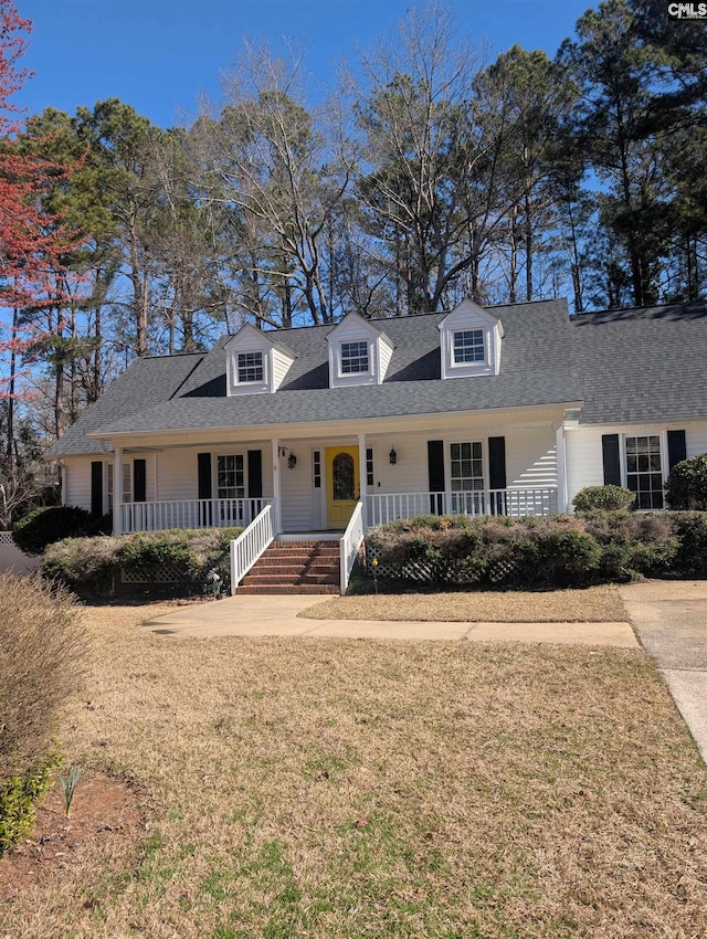 new england style home featuring a porch, a shingled roof, and a front lawn