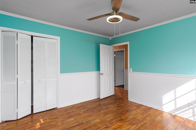 unfurnished bedroom with dark wood-type flooring, ornamental molding, a closet, and ceiling fan