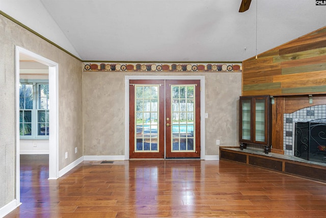 unfurnished living room with hardwood / wood-style flooring, vaulted ceiling, a tile fireplace, and french doors