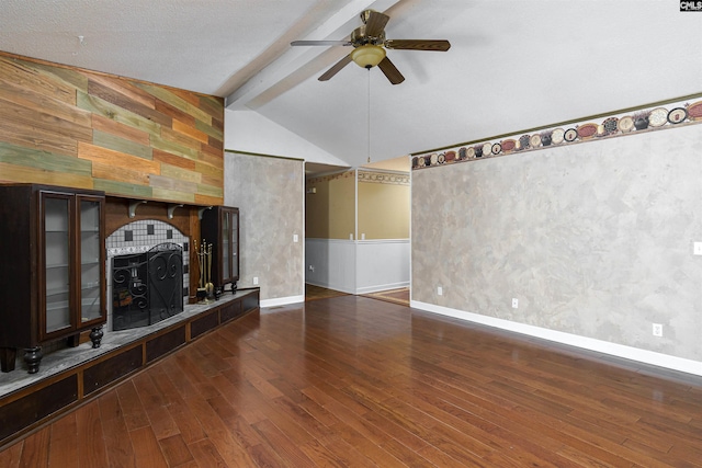 unfurnished living room featuring ceiling fan, dark hardwood / wood-style floors, a tile fireplace, and vaulted ceiling with beams