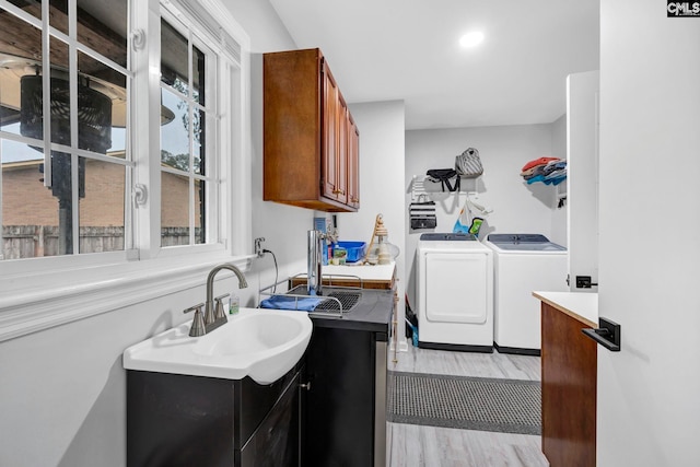 clothes washing area featuring cabinets, washing machine and clothes dryer, and light hardwood / wood-style floors