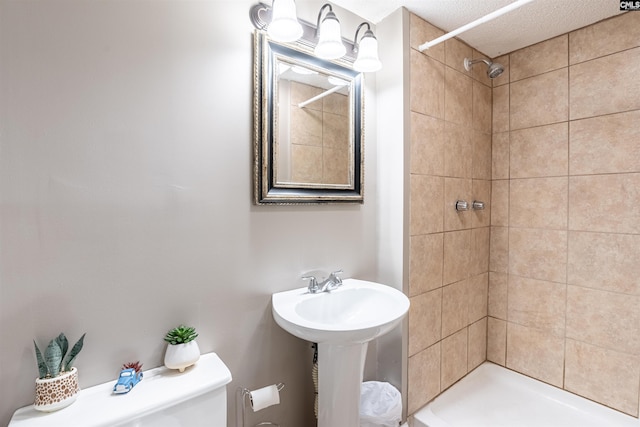 bathroom featuring tiled shower, toilet, and sink