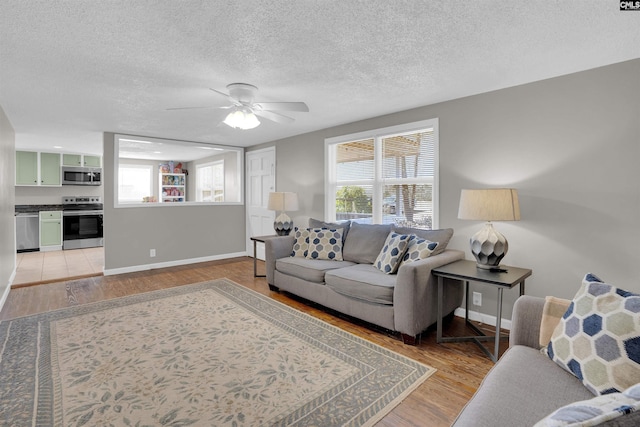 living room featuring ceiling fan, light hardwood / wood-style flooring, and a textured ceiling