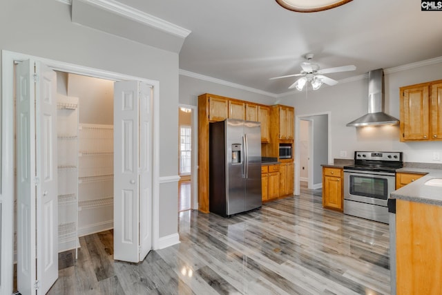 kitchen featuring wall chimney exhaust hood, light hardwood / wood-style flooring, ornamental molding, appliances with stainless steel finishes, and ceiling fan