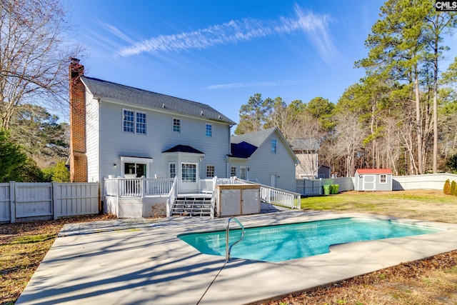 rear view of property featuring a pool side deck, a lawn, and a storage unit