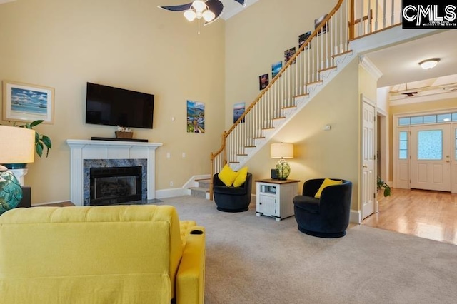 carpeted living room with ceiling fan, a towering ceiling, and a high end fireplace