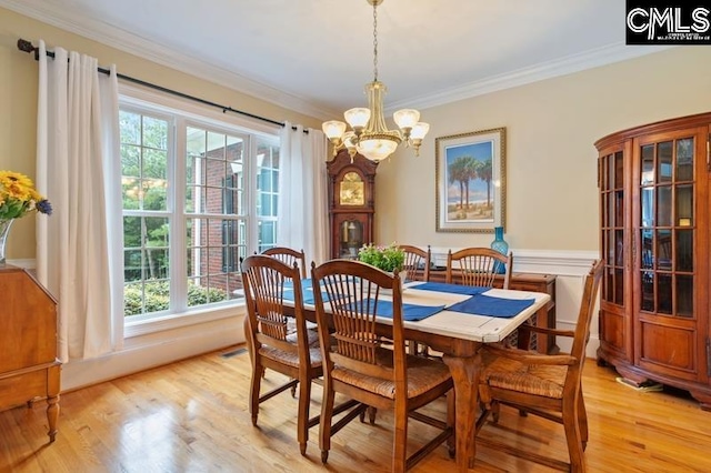 dining space featuring an inviting chandelier, ornamental molding, and light wood-type flooring