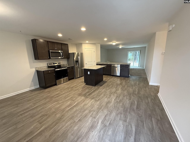 kitchen with stainless steel appliances, a kitchen island, dark brown cabinets, light stone counters, and wood-type flooring