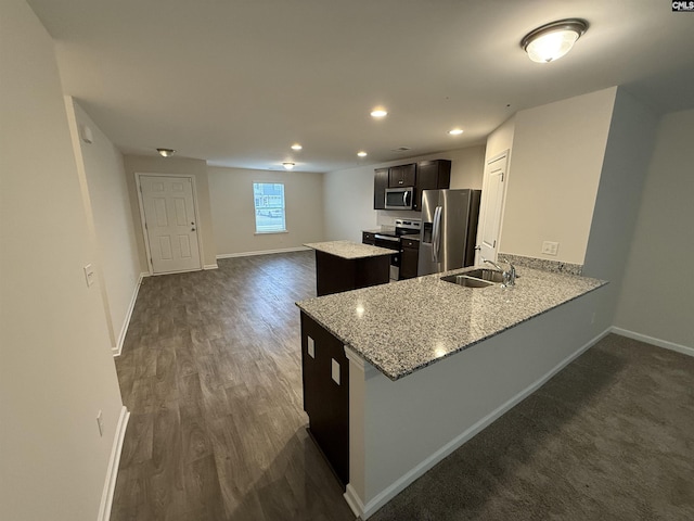 kitchen with appliances with stainless steel finishes, sink, light stone counters, a kitchen island, and kitchen peninsula