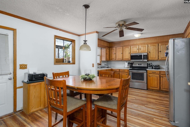 dining space featuring crown molding, ceiling fan, a textured ceiling, and light wood-type flooring