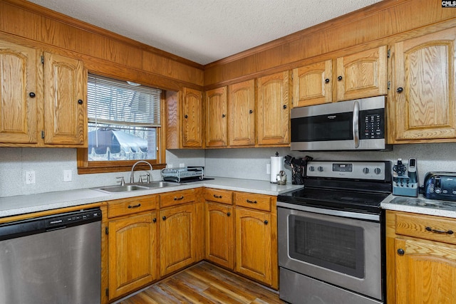 kitchen with appliances with stainless steel finishes, sink, light hardwood / wood-style flooring, and a textured ceiling