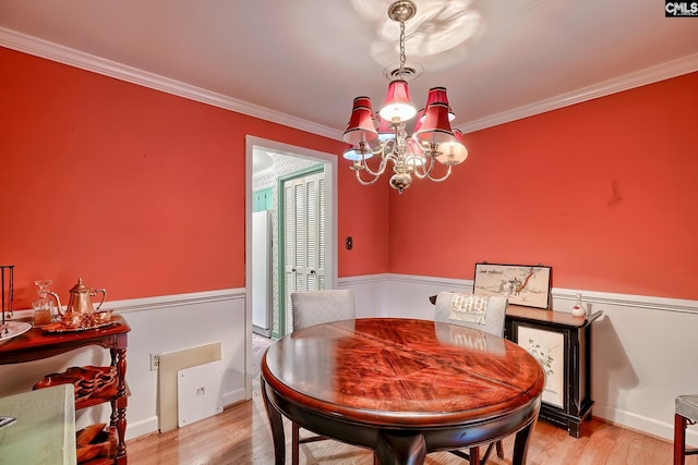 dining area with crown molding, light wood-type flooring, and an inviting chandelier