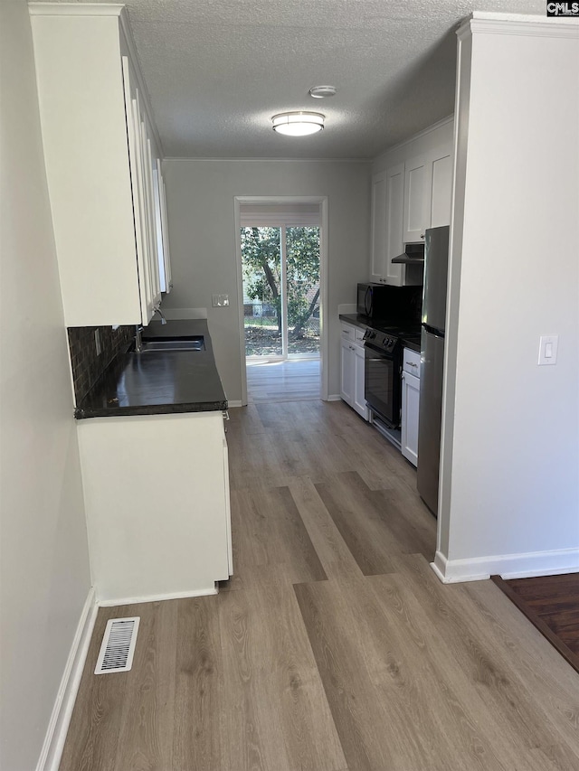 kitchen with sink, light hardwood / wood-style flooring, stainless steel refrigerator, black range with electric stovetop, and white cabinets