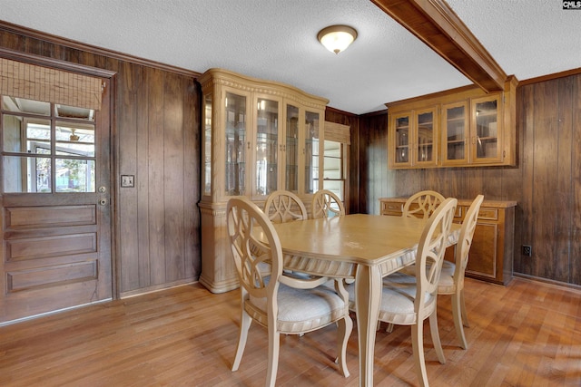 dining room with light hardwood / wood-style floors, a textured ceiling, and wood walls