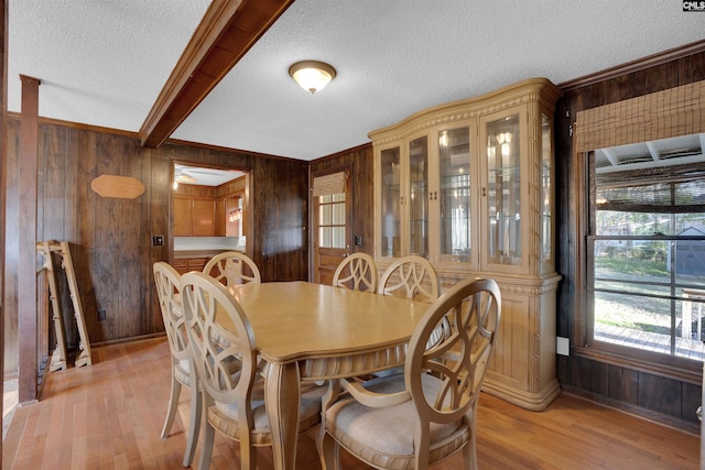 dining area with light hardwood / wood-style flooring, a textured ceiling, beam ceiling, and wood walls