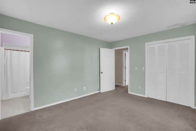 unfurnished bedroom with light carpet, a closet, a textured ceiling, and ensuite bathroom