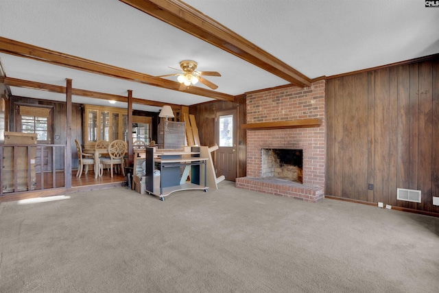 unfurnished living room with a fireplace, wood walls, carpet flooring, ceiling fan, and beam ceiling