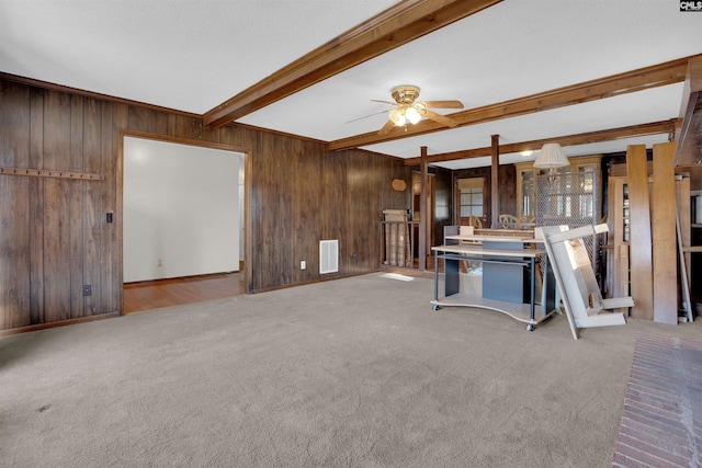 unfurnished living room featuring ceiling fan, light carpet, beam ceiling, and wood walls