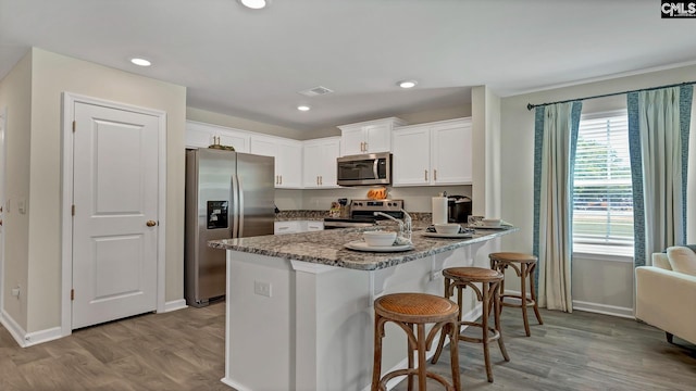 kitchen featuring white cabinetry, dark stone counters, kitchen peninsula, stainless steel appliances, and light hardwood / wood-style floors