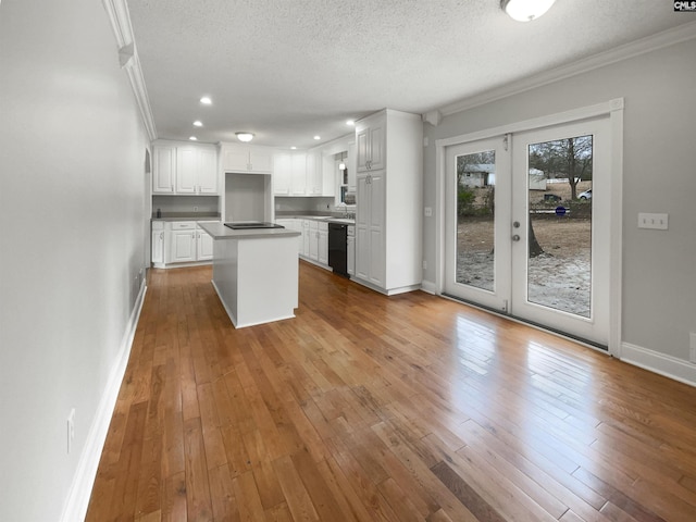 kitchen with white cabinets, a kitchen island, wood finished floors, crown molding, and black appliances