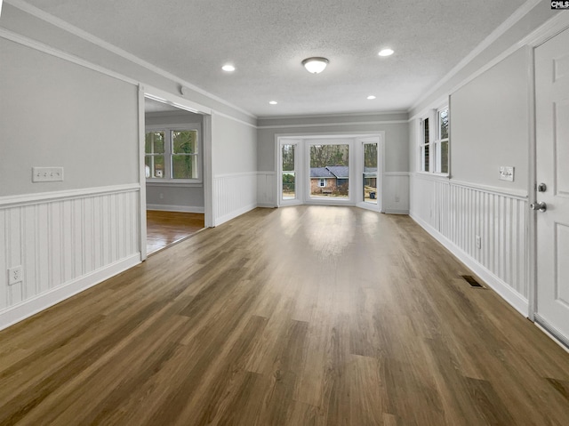 unfurnished living room featuring crown molding, dark wood finished floors, a textured ceiling, and wainscoting