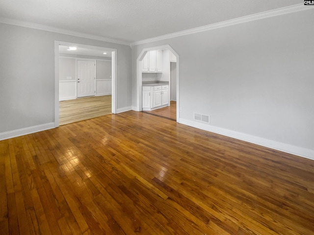 unfurnished living room with ornamental molding, arched walkways, visible vents, and wood finished floors