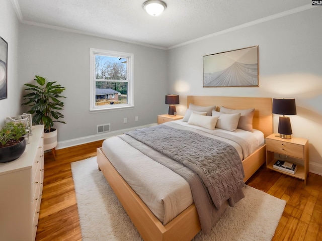 bedroom with ornamental molding, wood finished floors, visible vents, and baseboards