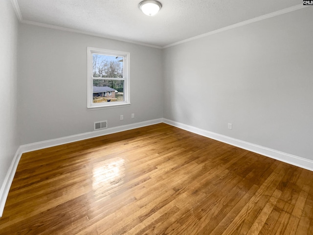 spare room with a textured ceiling, wood finished floors, visible vents, baseboards, and ornamental molding