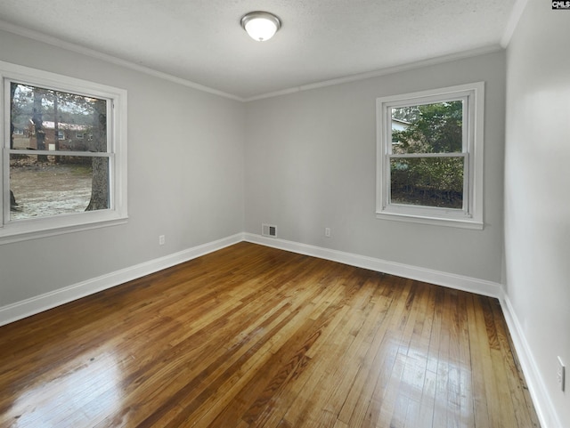 empty room with a textured ceiling, wood finished floors, visible vents, baseboards, and ornamental molding