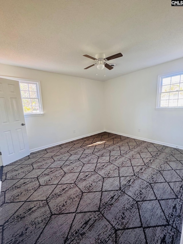 empty room with ceiling fan, a healthy amount of sunlight, and a textured ceiling