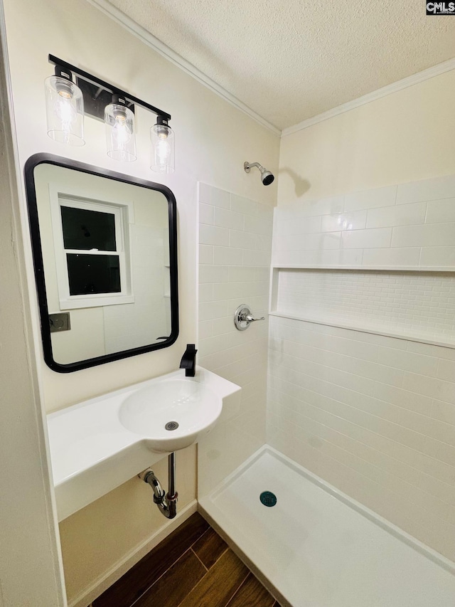 bathroom with sink, crown molding, a textured ceiling, a tile shower, and hardwood / wood-style floors