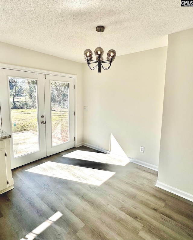 unfurnished dining area featuring a textured ceiling, a notable chandelier, dark hardwood / wood-style flooring, and french doors