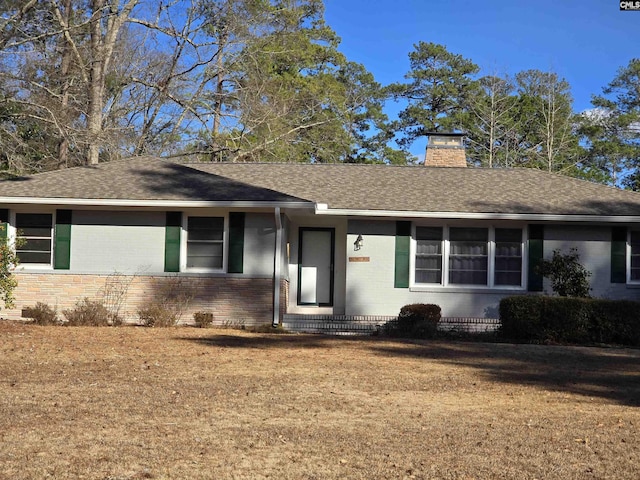 single story home featuring roof with shingles, brick siding, a chimney, and a front yard