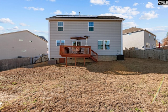 back of property featuring cooling unit, a wooden deck, a yard, and solar panels