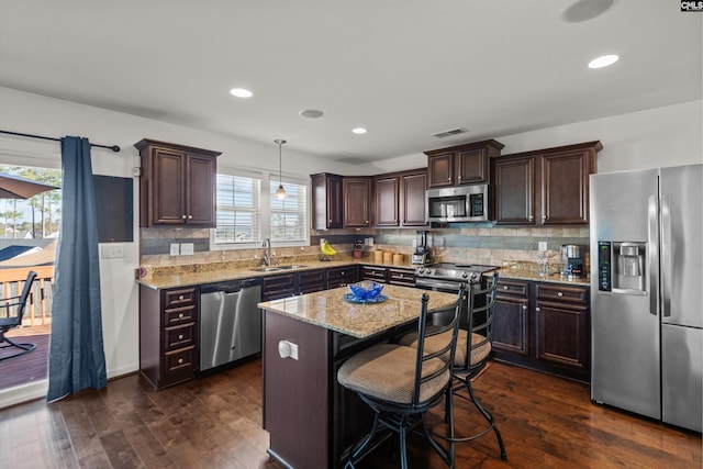 kitchen with sink, light stone counters, hanging light fixtures, a kitchen island, and stainless steel appliances