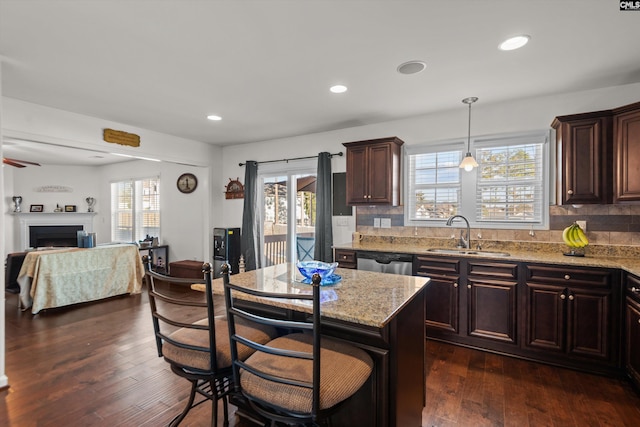 kitchen featuring sink, light stone counters, decorative light fixtures, dishwasher, and a kitchen island