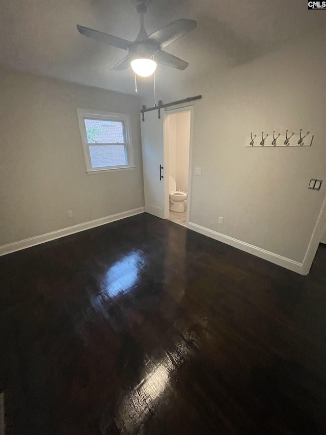 unfurnished bedroom with wood-type flooring, a barn door, and ceiling fan