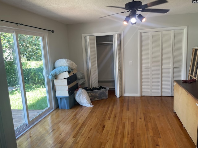 unfurnished bedroom with hardwood / wood-style floors, a textured ceiling, multiple closets, and ceiling fan