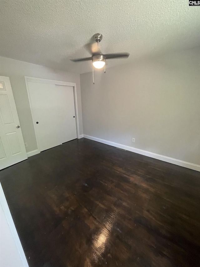 spare room featuring ceiling fan, dark wood-type flooring, and a textured ceiling