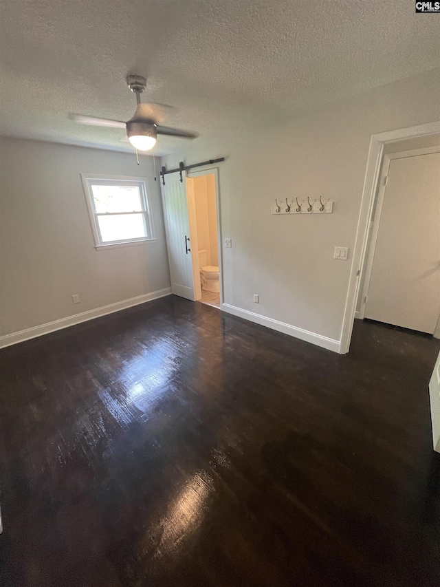 unfurnished room with ceiling fan, a barn door, a textured ceiling, and dark hardwood / wood-style flooring